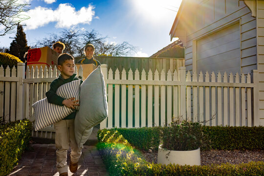 Children with mixed ethnicity carrying card boxes and pillows inside picket fence on moving day