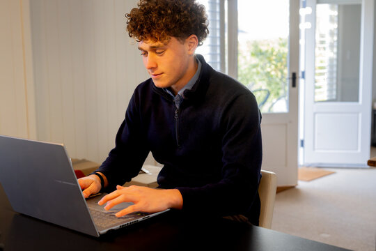 Teenage boy with curly hair doing homework using a laptop