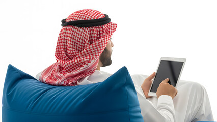 Arab man in traditional attire using a tablet while relaxing on a blue beanbag chair indoors.