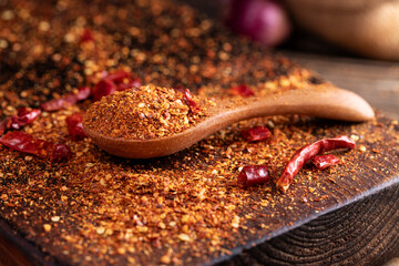 A close-up image of chili powder in a wooden spoon, spices for Asian cooking, arranged on a wooden table, conveying the concept of spicy food.