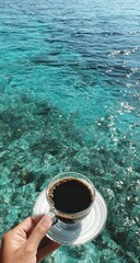 Hand holding coffee cup against vibrant turquoise ocean backdrop