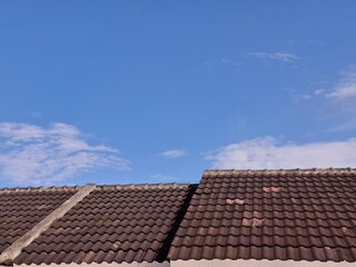 Fototapeta premium A clean view of brown clay roofing tiles against a bright sunny blue sky with light clouds, ideal for real estate, housing, and construction themes.