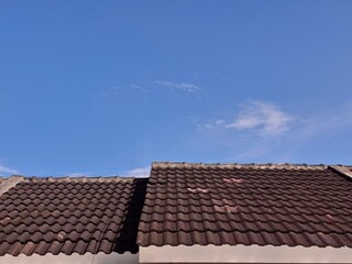 Fototapeta premium A clean view of brown clay roofing tiles against a bright sunny blue sky with light clouds, ideal for real estate, housing, and construction themes.