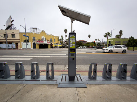 LOS ANGELES, CA, OCT 7, 2025: Bike share station with central information section, solar panel on top, multiple gray bike docks arranged in rows along city street