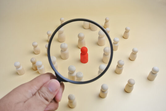 Magnifying glass highlighting a red wooden figure among white wooden