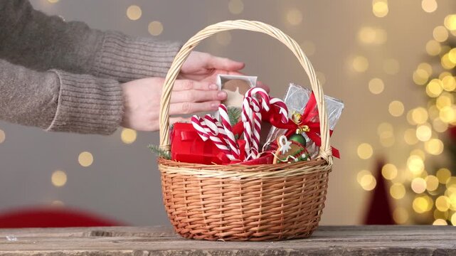 Merry Christmas and Happy New Year. Woman with gift basket full of sweets and festive decor at wooden table indoors, closeup