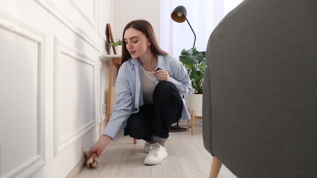 Woman wiping dust from baseboard at home
