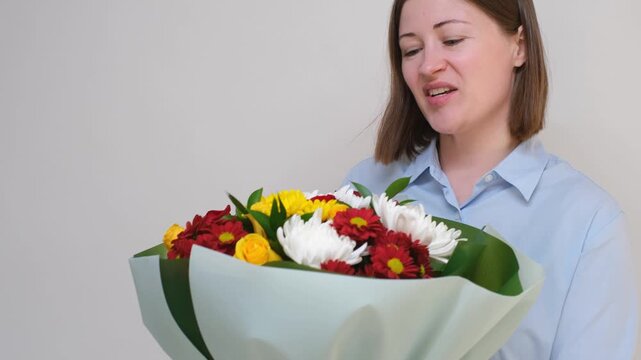 A young woman holds a chic bouquet of flowers of yellow roses and asters on dray background.
