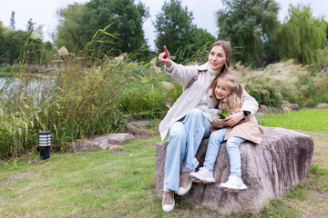 Mother and daughter sitting on a rock in a park and pointing at something