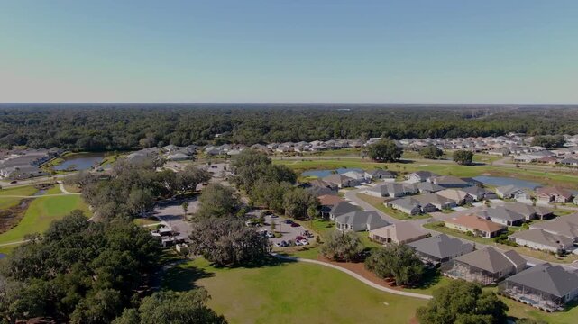 Descending drone shot over Edna&rsquo;s on the Green in The Villages, Florida, revealing nearby residential neighborhoods, green space, ponds, and distant forest under clear skies.