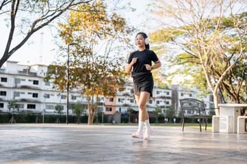 Fototapeta premium Asian woman in sportswear listening to music in headphone while running or jogging exercise in park