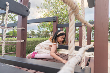 Obraz premium Excited Asian girl laughing happily on the high platform of a wooden playground structure