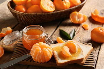 Fototapeta premium Jar of tasty tangerine jam with toasts and knife on wooden background