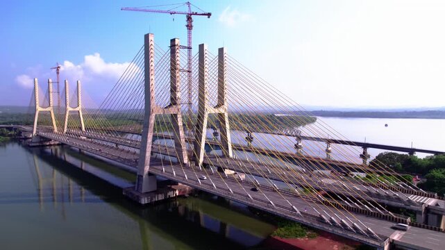Vehicles moving on large pylons bridge with river and tower crane at goa. day time, jib shot, drone shot, 4k.
