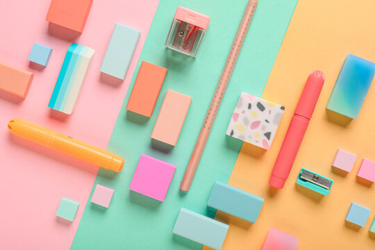 Different rubber erasers with pencil, sharpeners and markers on color background