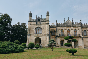 Castle style historic building with ornate stone facade and towers stands amid a neatly trimmed garden and mature trees, creating a dramatic, timeless architectural scene in daylight.