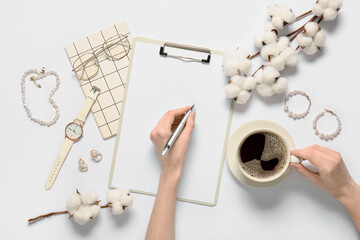 Female hands with clipboard, cup of coffee, cotton flowers, eyeglasses and jewelry on white...