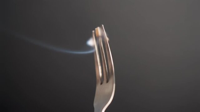 Silver fork with smoke coming out of the tines on a dark background.