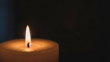 Single candle flame flickering in the darkness, casting a warm glow on its textured surface, evoking peace and introspection.