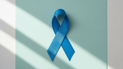 Symbol of hope: a satin blue ribbon with textured surface casts shadows on a soft teal background, representing awareness and support