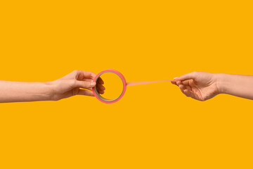Female hands with pink masking tape roll on yellow background