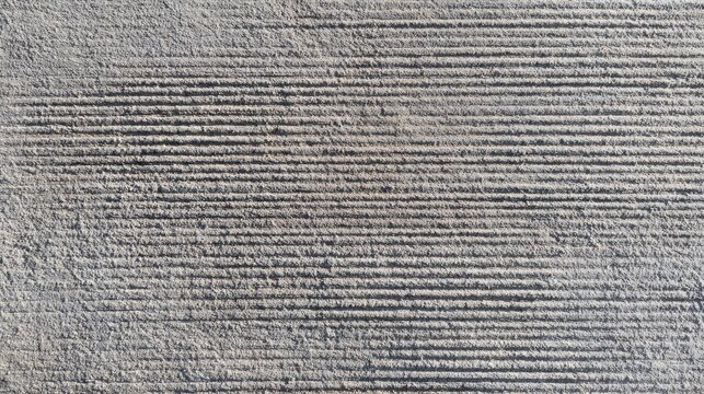 Brushed concrete surface texture, fine parallel broom marks across grey cement, sidewalk or pavement finish, tactile industrial background, uniform daylight 