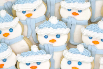 Close up on snowmen sugar cookies decorated with mashmallow fondant, candy eyes and nose, royal icing hat and scarf. Festive holiday treats.
