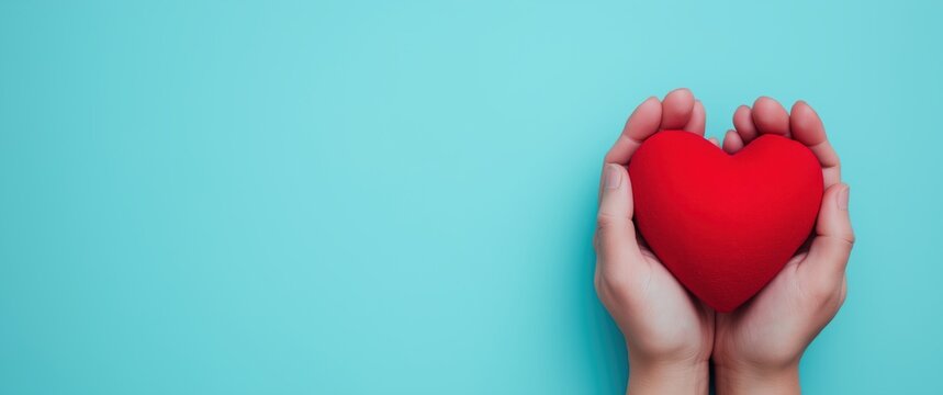 Hands holding a vibrant red heart on a turquoise background, symbolizing love, care, health, and charitable giving with copy space