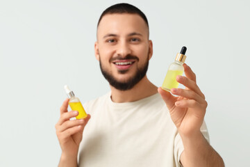 Handsome young man with bottles of vitamin E serum on grey background