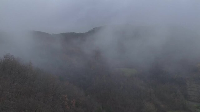 Aerial of low autumn clouds drifting over the Val Tolla forest near Castelletto, revealing the colorful beech and chestnut canopy that once belonged to the historic Abbey of Val Tolla