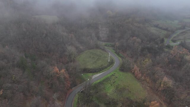 Winding road from Castelletto to Vezzolacca as it disappears into the low autumnal clouds of the Val Tolla, highlighting the dense chestnut forests and Romanesque heritage of the Piacenza Apennines.