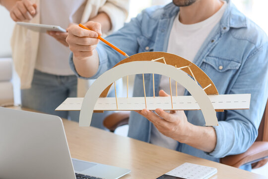 Male architect and his assistant working with 3D model of bridge at table in office, closeup