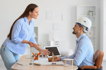 Fototapeta premium Male architect with assistant measuring house model at table in office