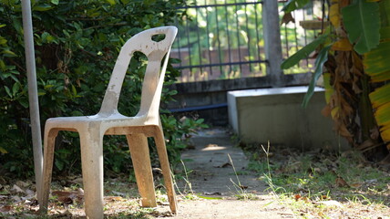 Lone Plastic Chair in a Garden Path Surrounded by Lush Green Foliage and Light