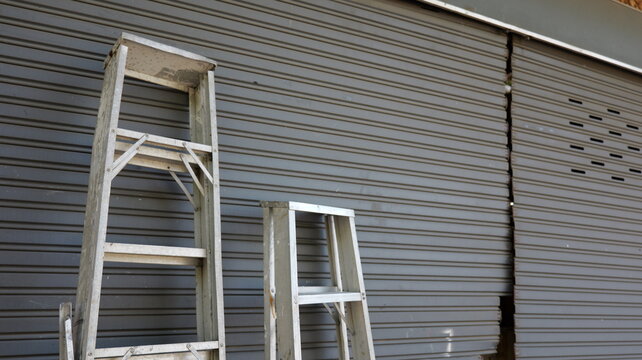 Wooden Ladders Leaning Against Gray Shuttered Storefront with Visible Crack