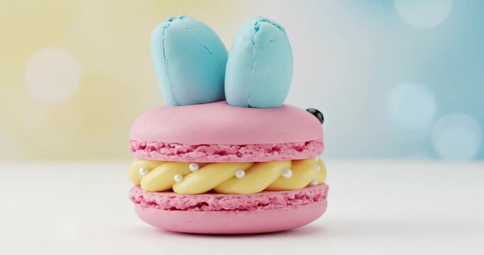 Cute pastel macaron shaped like a bunny with blue ears, set against a soft blurred background