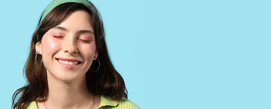 Happy young woman with face piercing on blue background with space for text