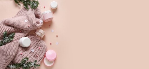 Jars of cream, Christmas decorations and warm winter clothes on pink background with space for text
