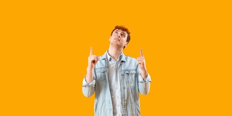 Young redhead man pointing upward on yellow background