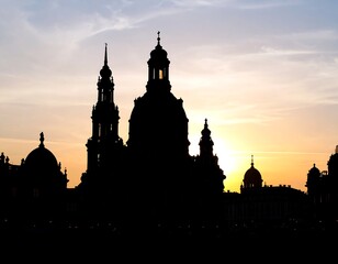 Silhouette of grand architecture against a soft sunset sky. Buildings are dark, with spires and domes silhouetted in the warm light