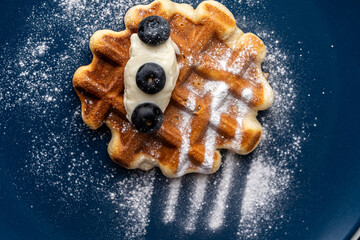 Close-up: Belgian waffles or dessert with white cream and blueberries sprinkled with powdered sugar...