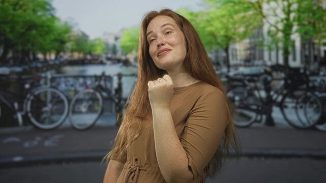 Smiling woman raising fist on canal street by water in amsterdam under bright sunlight; determination.