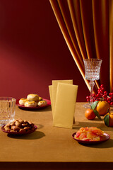 A festive Chinese New Year still life with fruits, cakes, glass cups and yellow lucky envelopes placed on yellow table. Space for product design, vertical frame, front view
