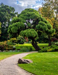 Serene outdoor scene featuring a winding path, lush greenery, and a prominent, uniquely shaped tree under a cloudy sky