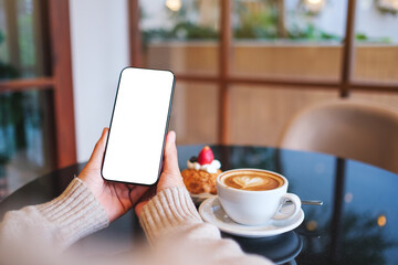 Mockup image of a woman holding and using mobile phone with blank desktop screen in cafe