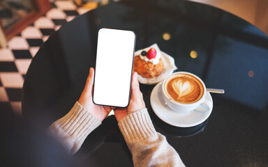 Top view mockup image of a woman holding and using mobile phone with blank desktop screen in cafe