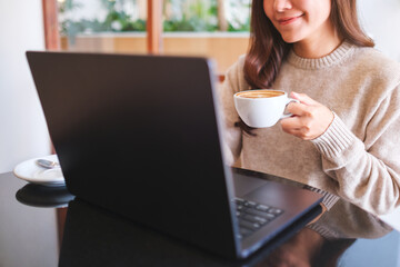 Closeup image of a woman working on laptop computer while drinking coffee in cafe