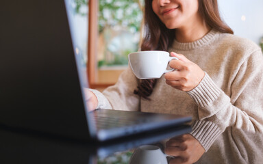 Closeup image of a woman working on laptop computer while drinking coffee in cafe