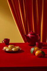 Vertical Lunar New Year composition with red table, cakes, tea pot, and traditional snacks. The simple background allows space for branding and holiday messaging