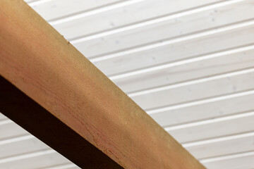 Rough natural wooden beam is under white ceilinfg made of planks